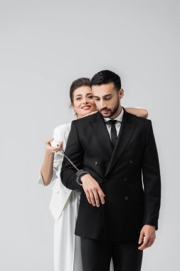 Müslüman erkek arkadaşının yanında elleri kelepçeli, gülen gelin gri alanda izole edilmiş. 