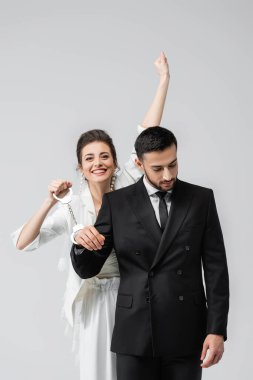 Arap damadın kelepçelerini tutan mutlu gelin gri alanda izole edilmiş. 