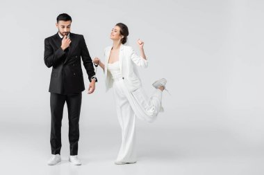 Gelinlik giymiş neşeli bir kadın beyaz arka planda Müslüman erkek arkadaşının kelepçelerini tutuyor.