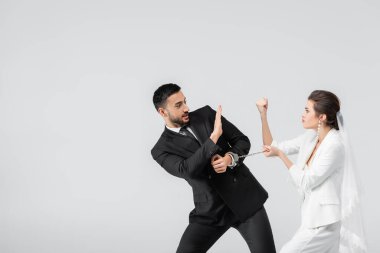 Elleri kelepçeli gelin, yumruğunu Müslüman damada gösteriyor. Dükkan jestini gri renkte gösteriyor. 