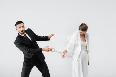 Müslüman damat kelepçe takıyor ve üzgün gelin peçesi gri renkte izole edilmiş. 