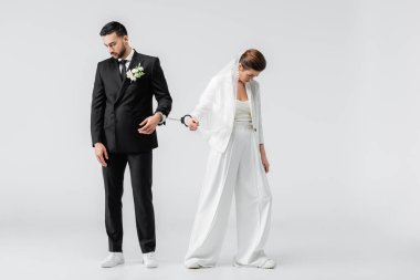 Beyaz arka planda kelepçeli ırklar arası üzgün damat ve gelin.