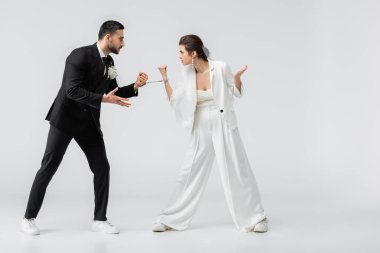 Aggressive interracial bride and groom in handcuffs looing at each other on white background clipart