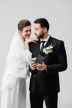 Gülümseyen gelin, gri renkte cüzdanı ve parası olan Arap damadı kucaklıyor. 