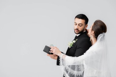Duvak takmış gelin, gri renkte izole edilmiş Arap damadın cüzdanından para konuşuyor. 
