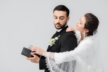 Olumlu gelin, gri renkte izole edilmiş Arap damadın cüzdanından para alıyor. 
