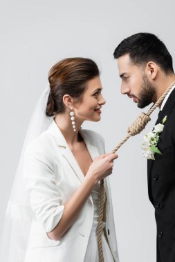 Gülümseyen gelinin, gri renkte izole edilmiş Müslüman damadın boynuna halat çekişi. 