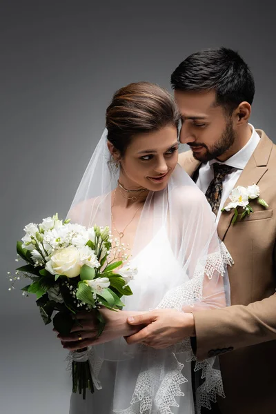 Noivo Muçulmano Abraçando Noiva Sorridente Com Buquê Casamento Isolado Cinza — Fotografia de Stock