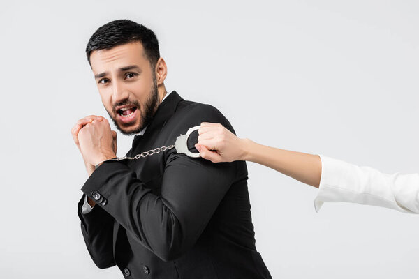 Испуганный мусульманский жених смотрит в камеру рядом с невестой с наручниками, изолированными на сером 