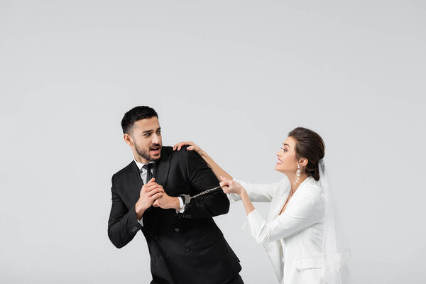 Испуганный арабский жених в наручниках, смотрящий на веселую невесту, изолированную от серых 