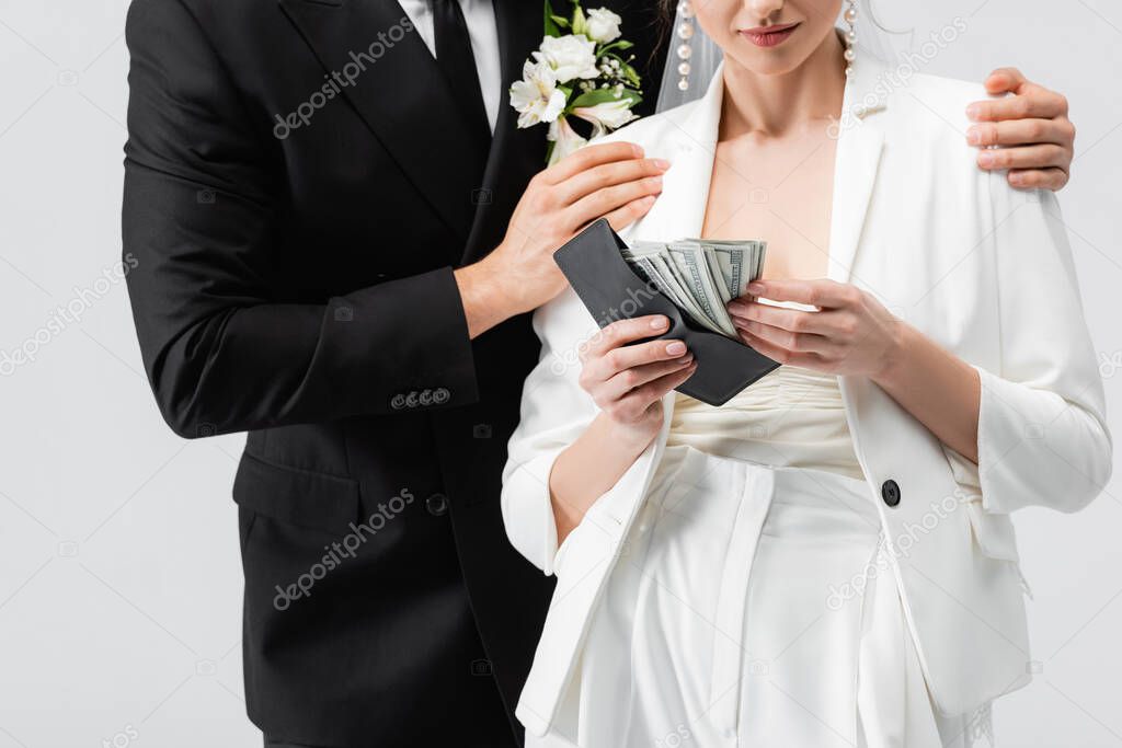 Cropped view of groom hugging bride with currency and wallet isolated on grey 