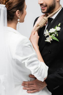 Boynunda düğümle gülen damat. Gri renkte izole edilmiş gelini kucaklıyor. 