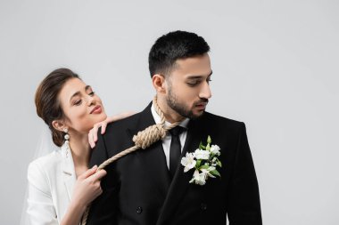 Gülen gelin, gri üzerine izole edilmiş Müslüman erkek arkadaşının boynunda düğümünü tutuyor. 