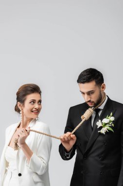 Gülümseyen gelin, gri renkte izole edilmiş Müslüman damadın boynunda kaygan bir düğümle ip tutuyor. 