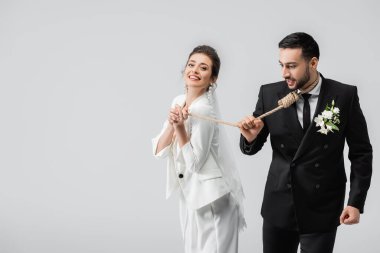 Gri yolda izole edilmiş Müslüman erkek arkadaşının boynuna ip bağlayan neşeli gelin. 