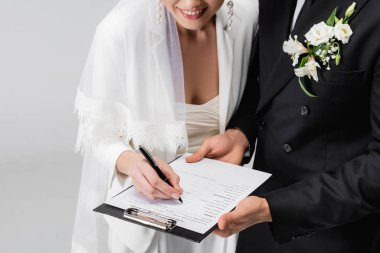 Gülümseyen gelinin damada yakın bir yerde izole edilmiş bir evlilik sözleşmesi imzalaması görüntüsü. 