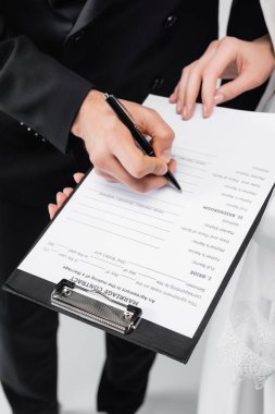 Cropped view of groom signing marriage contract on clipboard near bride on grey background  clipart