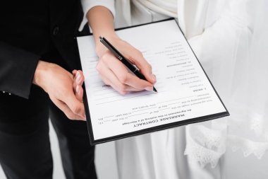 Cropped view of couple signing marriage contract isolated on grey  clipart