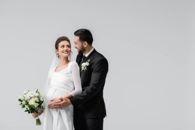 Neşeli Müslüman adam, gri renkli çiçekli hamile geline bakıyor. 
