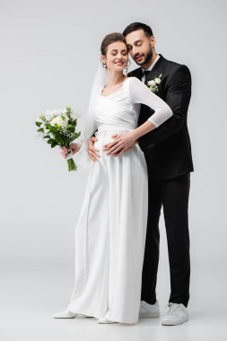 Arap damat gri arka planda hamile gelini kucaklıyor. 