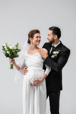 Gri renkte izole edilmiş düğün buketiyle hamile gelini kucaklayan Müslüman damat. 