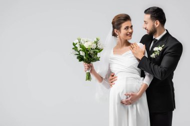 Genç Müslüman adam, neşeli hamile geline sarılıyor. Gri yolda izole edilmiş. 