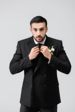 Müslüman damat kravatı düzeltiyor ve gri kameraya bakıyor. 