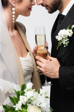 Zarif yeni evli çiftin yüz yüze duran ve gri üzerine izole şampanya bardakları tutan görüntüsü.