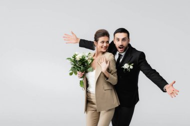 Şaşırmış müslüman adam kollarını açmış mutlu, zarif gelin gri üzerinde yalnız duruyor.