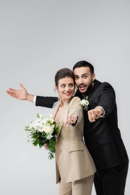 Heyecanlı, çok ırklı yeni evli çift gri renkte izole edilmiş alyanslar gösteriyor.