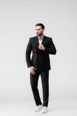 Siyah takım elbiseli ve spor ayakkabılı genç bir Arap gri üzerinde dikilirken gözlerini kaçırıyor.