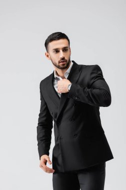 Siyah takım elbiseli genç bir Arap, gri üzerinde yalnız poz verirken gözlerini kaçırıyor.