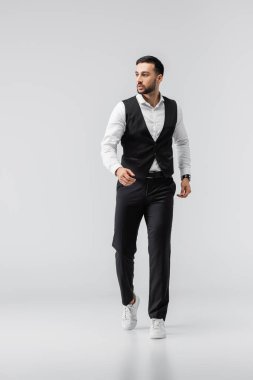 Moda kıyafetleri ve spor ayakkabıları içinde gri yolda yürüyen modaya uygun Arap bir adam.