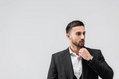 Genç, esmer, Arap bir adam, yakasına dokunuyor. Gözünü griye dikmiş, başka tarafa bakıyor.