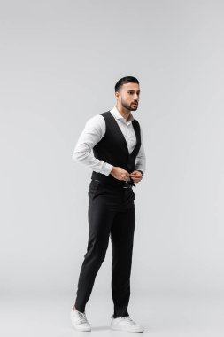 Modaya uygun Müslüman adam, gri gömleğini iliklerken başka tarafa bakıyor.