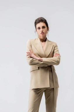 sensual woman in trendy pantsuit posing with crossed arms isolated on grey clipart