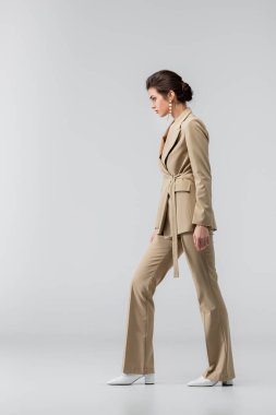 full length of woman in stylish pantsuit standing on grey, side view clipart