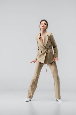 Bej takım elbiseli, gri renkli kameraya bakan şehvetli kadının tam boy görüntüsü.