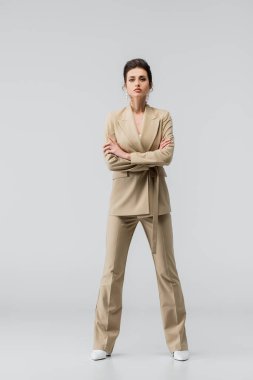 Esmer, modaya uygun bir kadın kameraya bakarken gri kolları çapraz duruyor.