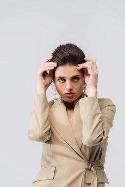 Kameraya bakan zarif genç bir kadın. Elleri başının yakınında, gri renkte poz veriyor.