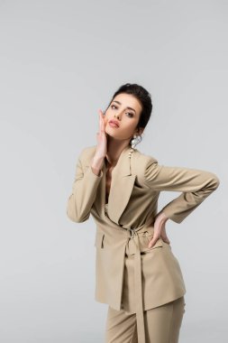 Yüze dokunan modaya uygun bir kadın, elleri kalçasında gri renkte poz veriyor.