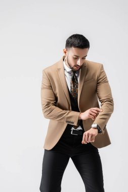 Modaya uygun bir Arap adam, gri renkte poz verirken kol saatini kontrol ediyor.