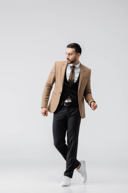 Zarif giysiler ve spor ayakkabılar içindeki genç Müslüman adamın gri üzerinde duruşu.