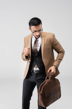 Gri üzerinde deri çantayla gezen modaya uygun takım elbiseli genç bir Arap.