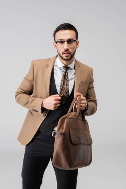 Gri üzerinde deri çanta taşıyan şık elbiseli genç bir Arap.