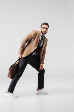 Gri renkli deri çantayla poz verirken kameraya bakan modaya uygun Müslüman adamın tam boy görüntüsü