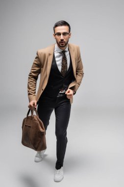 Gri renkli deri çantayla koşan zarif Müslüman adamın tam boy görüntüsü.