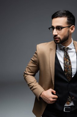 Bej ceketli ve siyah yelekli genç bir Arap griye bakıyor.