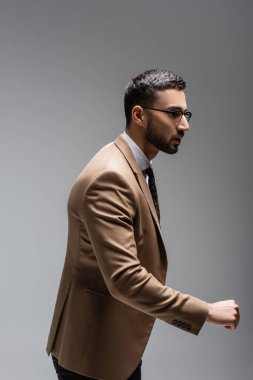 Bej renkli, modaya uygun ceketli genç müslüman gri yolda tek başına yürürken başka tarafa bakıyor.