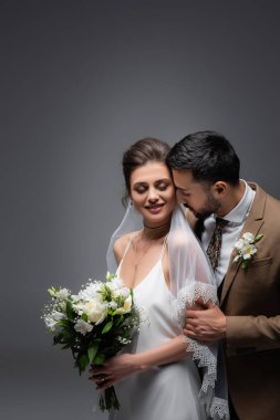 Mutlu gelini kucaklayan Arap adam, gri renkte düğün buketi tutuyor.